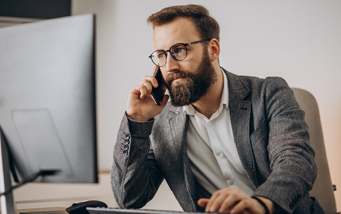 Homme à lunettes au téléphone qui regarde un ordinateur